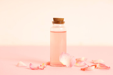 Obraz na płótnie Canvas Bottle of natural cosmetic oil and rose petals on pink background