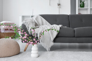 Vase with blooming branches on floor in living room
