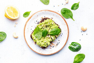 Avocado toasts with spinach and cashew nuts sprinkled with sesame seeds on white table background, top view - 792153370