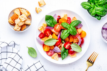 Summer italian salad with stale bread, tomatoes, red onion, olive oil, salt and green basil, white table background, top view