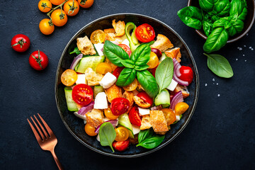 Frash vegetable salad with stale bread, tomatoes, cucumber, cheese, onion, olive oil, sea salt and green basil, black table background, top view - 792153991