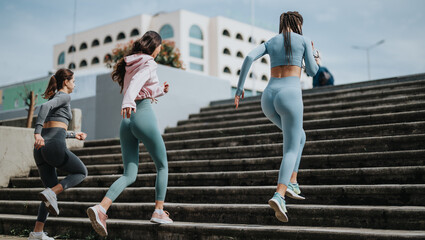 Active young women in workout attire exercising together by running up city stairs, showcasing health and companionship.