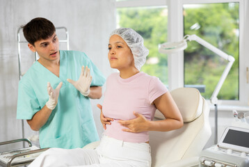 Young male doctor consulting young female patient on breast augmentation in clinic