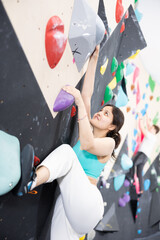 Young Asian woman climbs steep artificial wall in sports complex and trains endurance and muscle...