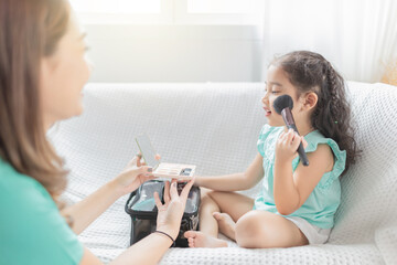 attractive asian children learning use cosmetic , she use brush paint on her cheek, make up artist , children development, family activity