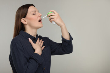 Woman using throat spray on grey background, space for text