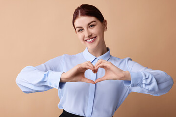Happy young woman showing heart gesture with hands on beige background