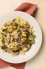 Vegetarian pasta with mushrooms, parsley, string beans and cheese on orange textured table, top view