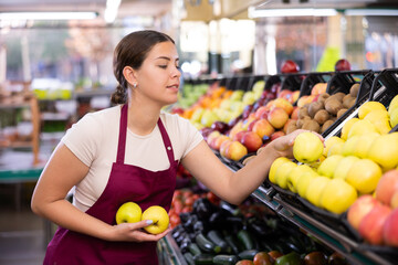 Positive female supermarket salesperson setting out apples on shelves