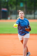 Young woman pitching fluorescent yellow softball on field during game.