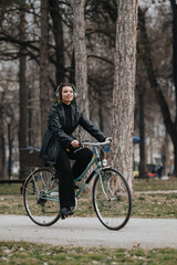 Obraz premium Confident female professional riding a bicycle with headphones in an urban park setting, exemplifying eco-friendly commute.