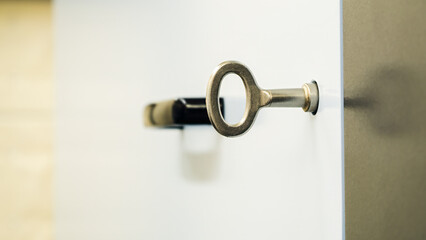 Symbolizing access and security, a modern silver key is inserted into a door lock, with a blurred black handle in the background adding depth to the image