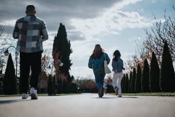 A group of friends bounding down a path lined with neat trees under a bright sky, engaging in...