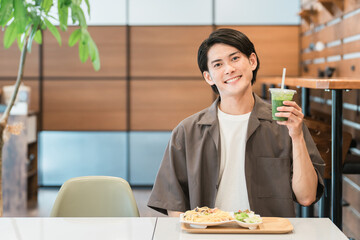 カフェでランチを食べながらグリーンスムージーを飲む若い男性（酵素・デトックス・食物繊維・健康食品）
