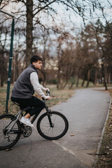 A teenage boy riding his bicycle on a park path surrounded by trees with autumn leaves.
