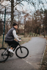Fototapeta premium A teenage boy riding his bicycle on a park path surrounded by trees with autumn leaves.