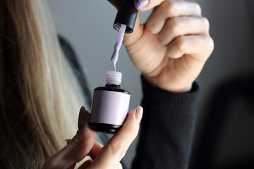 A blonde girl holds open nail polish in her hand. Close-up photo