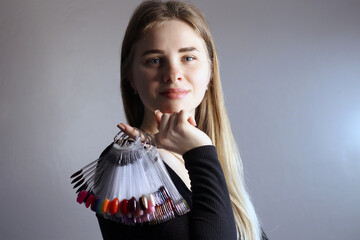 A blonde girl holds in her hand a palette with samples of nail polishes. Large selection of gel polish colors. Color display on the ring. Close-up photo
