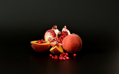 Broken ripe pomegranate fruit with seeds and pieces of peach on a black abstract background.