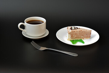 A piece of mint cream cheesecake on a plate, a fork and a cup of hot black coffee.