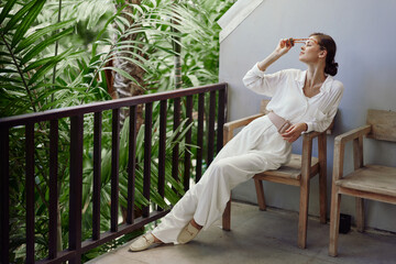 Tropical Balcony Bliss A Smiling Woman Embraces Travel and Relaxation, Enjoying the Sunshine on a...