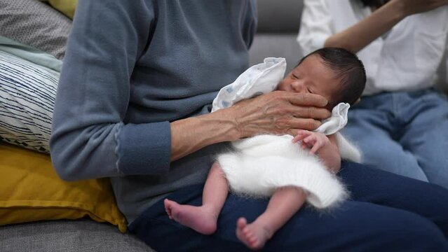 A Taiwanese grandmother in her 70s is making her 8-day-old baby in a white costume burp. ７０代の台湾人の祖母が白い衣装を来た生後８日の赤ちゃんにゲップさせている