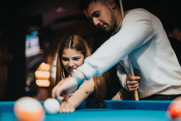 A man and woman share a playful moment while playing pool, surrounded by the warm ambiance of a...