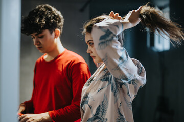 A casual moment captured as a young woman ties her hair and a young man stands focused beside her.