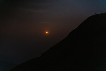 Obraz premium A bright yellow sun is shining in the sky over a dark mountain