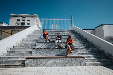 Three business professionals engaged in a discussion outdoors, seated on steps in a city...