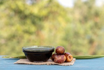 Date Palm Liquid Jaggery in a Glass Bowl or Phoenix Dactylifera Fruit with Leaves on Burlap Fabric Isolated on Wooden Table with Copy Space