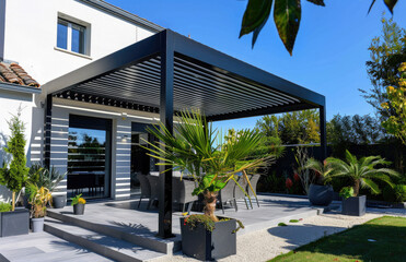 Design of a white minimalist and stylish garden canopy with slats on the terrace of an elegant modern house in France. The black steel structure frames the plants and blue sky.