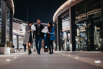 Business colleagues in a casual meeting while walking outside an office building decorated with festive lights at night.