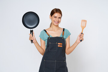 Young woman wearing kitchen apron cooking and holding pan and spatula isolated on white background. - obrazy, fototapety, plakaty