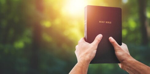 Christian holds bible book in hands with beautiful sunset.