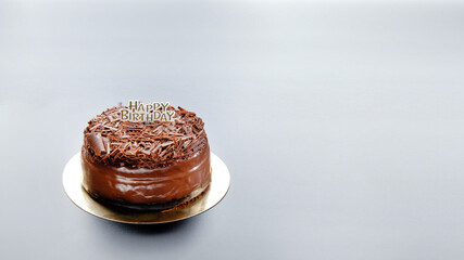 A dark black forest chocolate cake with a Happy Birthday sign sits on a black background