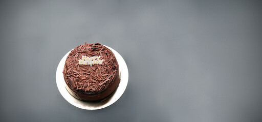 A dark black forest chocolate cake with a Happy Birthday sign sits on a black background