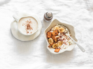Delicious breakfast, brunch - cottage cheese with banana, sour cream, crackers, chocolate and cappuccino on a light background, top view