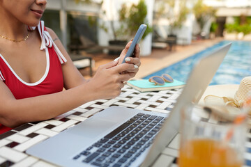Cropped image of woman in swimsuit answering text messages and emails when working by pool