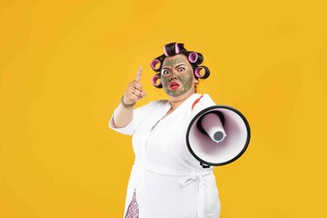 Portrait of a fat housewife wearing a natural mask and holding a megaphone isolated on a yellow...