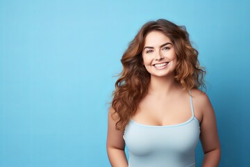 Obraz na płótnie Canvas smiling curvy woman looking at camera, standing against blue background, chubby, overweight 