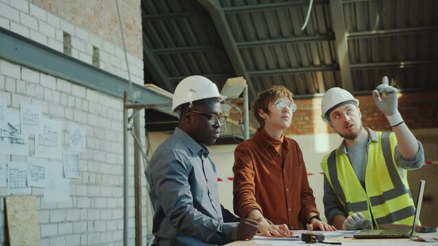 Young woman discussing floor plan and building process with Black contractor and Caucasian technician at construction site