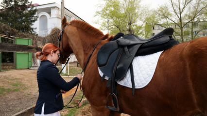 Equestrian tending to saddled horse, outdoor setting.