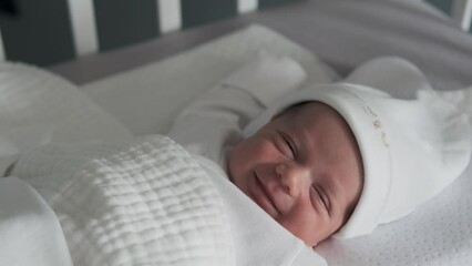 The beautiful 2 week old baby infant is smiling while sleeping in crib. Close-up portrait	
