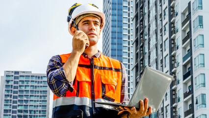 Contractor, Young man engineer checking information from laptop and commands with talking on radio call with colleague, Foreman working on building site, urban development in city