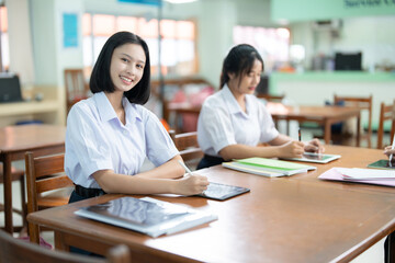 A short-haired Asian female student with a cute smile is the student body president. Have knowledge, be diligent and study hard. Read books and study online with laptops in the library.