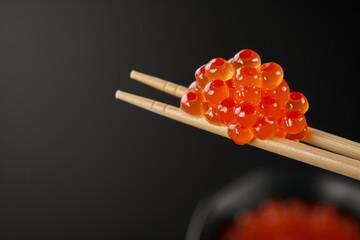 Red caviar on sushi chopsticks alone black backdrop