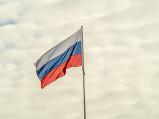 Russian tricolor flag waving in the wind against a blue sky.