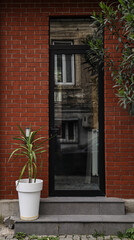 Front door, black front door with brown red wall, light fixtures and green potted plants. Front Door Frame and Greenery. Batumi, Georgia. Metaxa street. modern building exterior. private house, home.