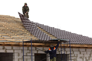 Workers install tiles on the roof of a house in winter - 792415953